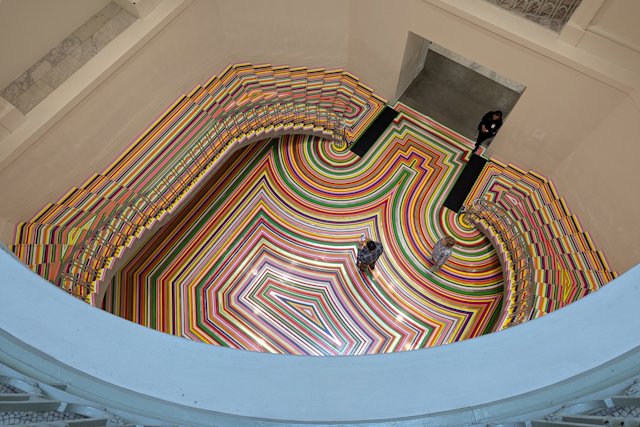 stairs and floor covered in bright colorful stripes, looking down from upper floor over the railing