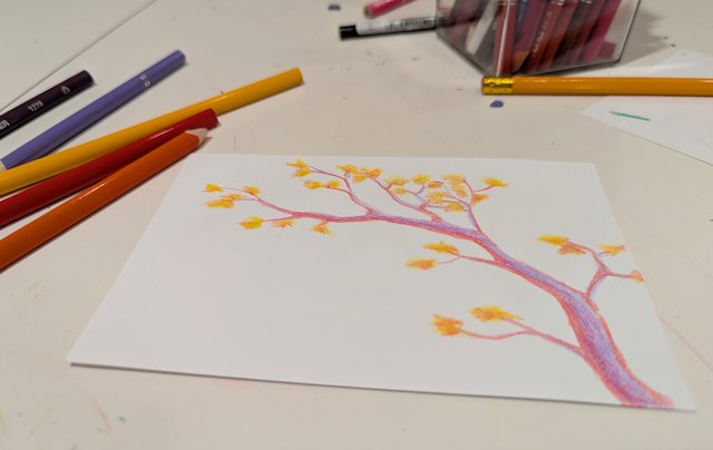 A drawing of a tree in purple, red, and yellow next to colored pencils on a table