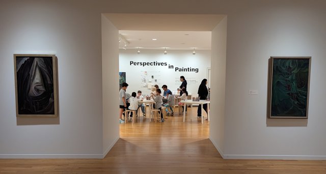 Looking through an opening with art on each side is an area with lots of kids at tables for drawing