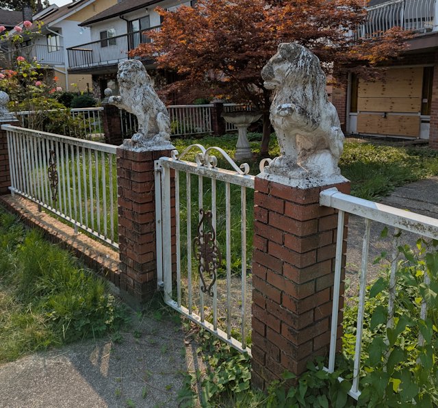 two lions statues sit atop brick pillars on each side of a front gate