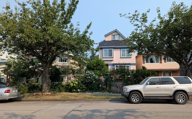 houses across a street with a parked SUV, trees flowers grow around the front yard fences