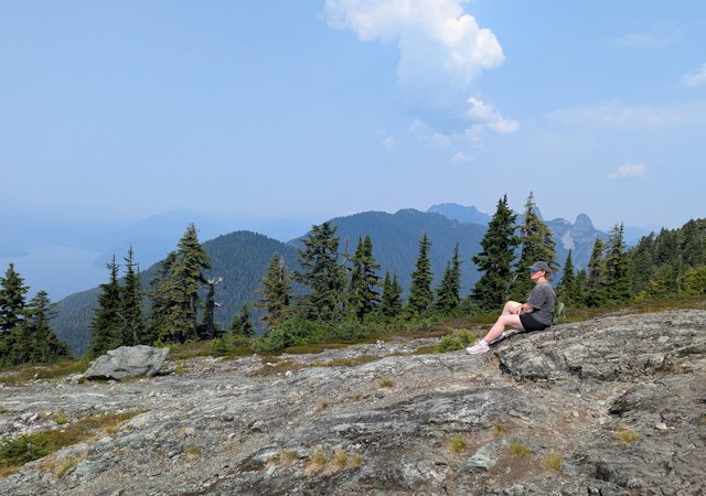 Stacey sitting on the rock at Cypress Moutain with peaks and clouds fading into blue behind her