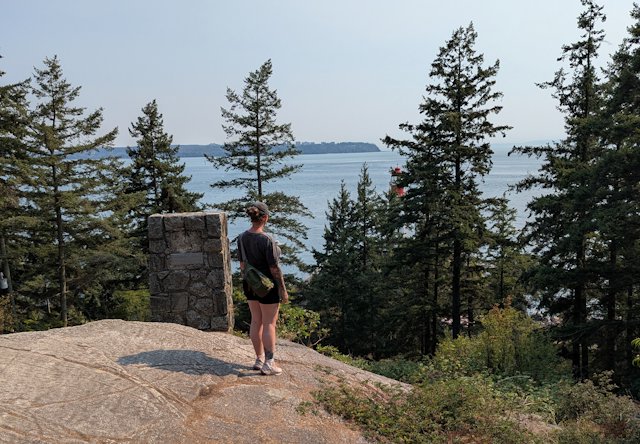 Stacey looks out at the lighthouse standing next to a stone recording lighthouse keepers