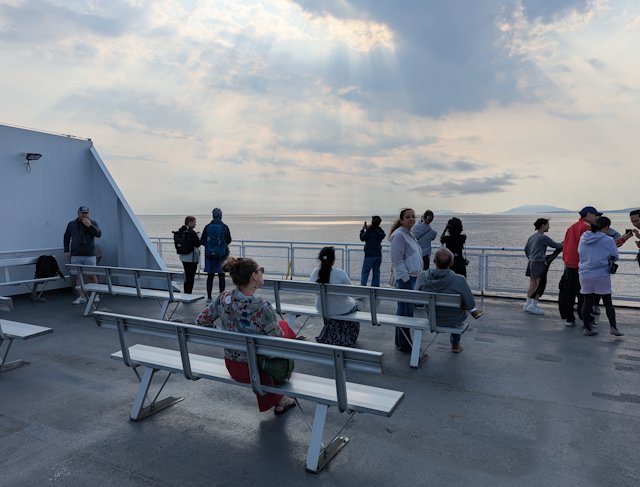 Stacey sits on the top deck with sunbeams streaming down between the clouds